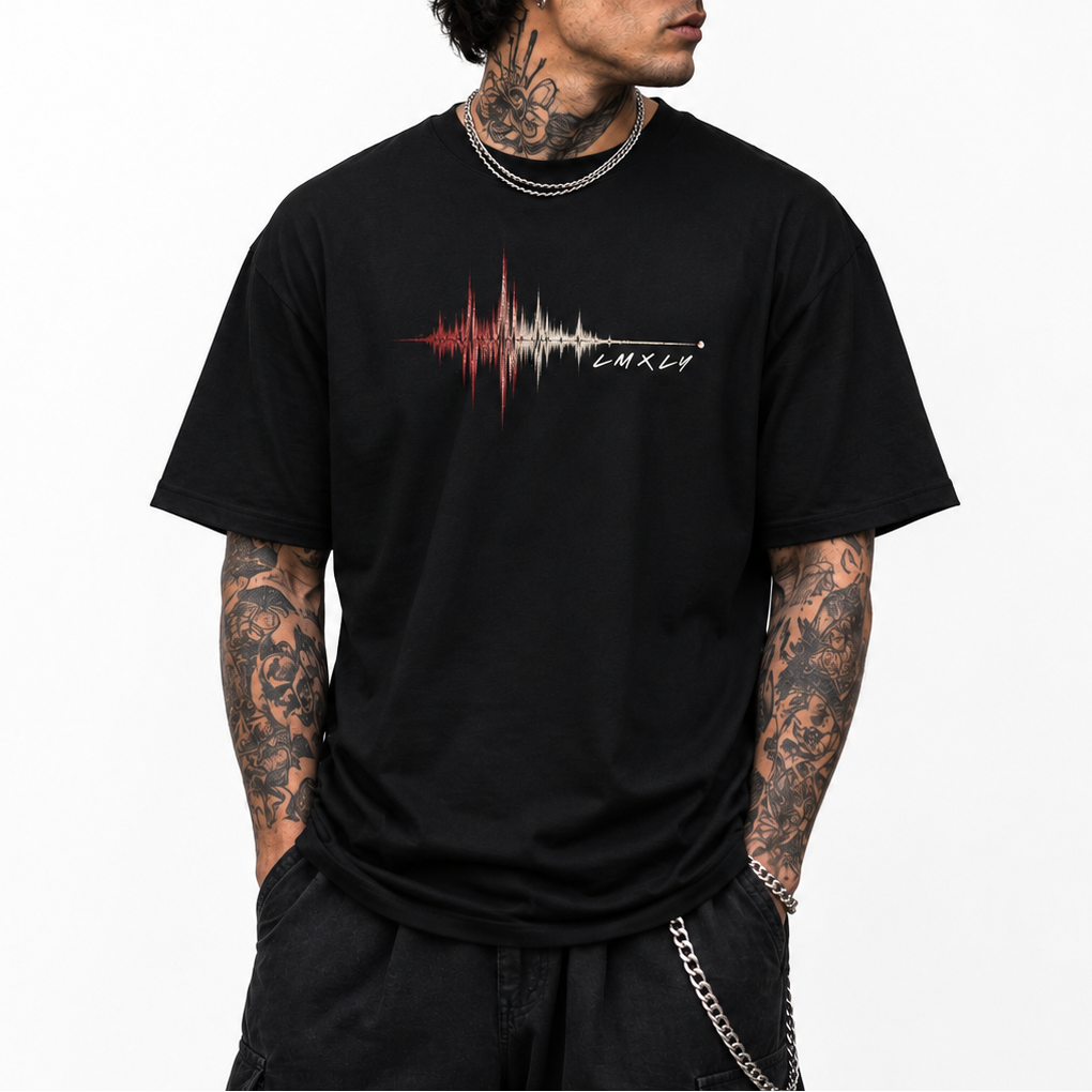 A man wearing a black crewneck t-shirt with a red and white soundwave graphic and the text 'LMXLY' on the chest, paired with a black baseball cap, black pants, and silver chain accessories, set against a plain white background.